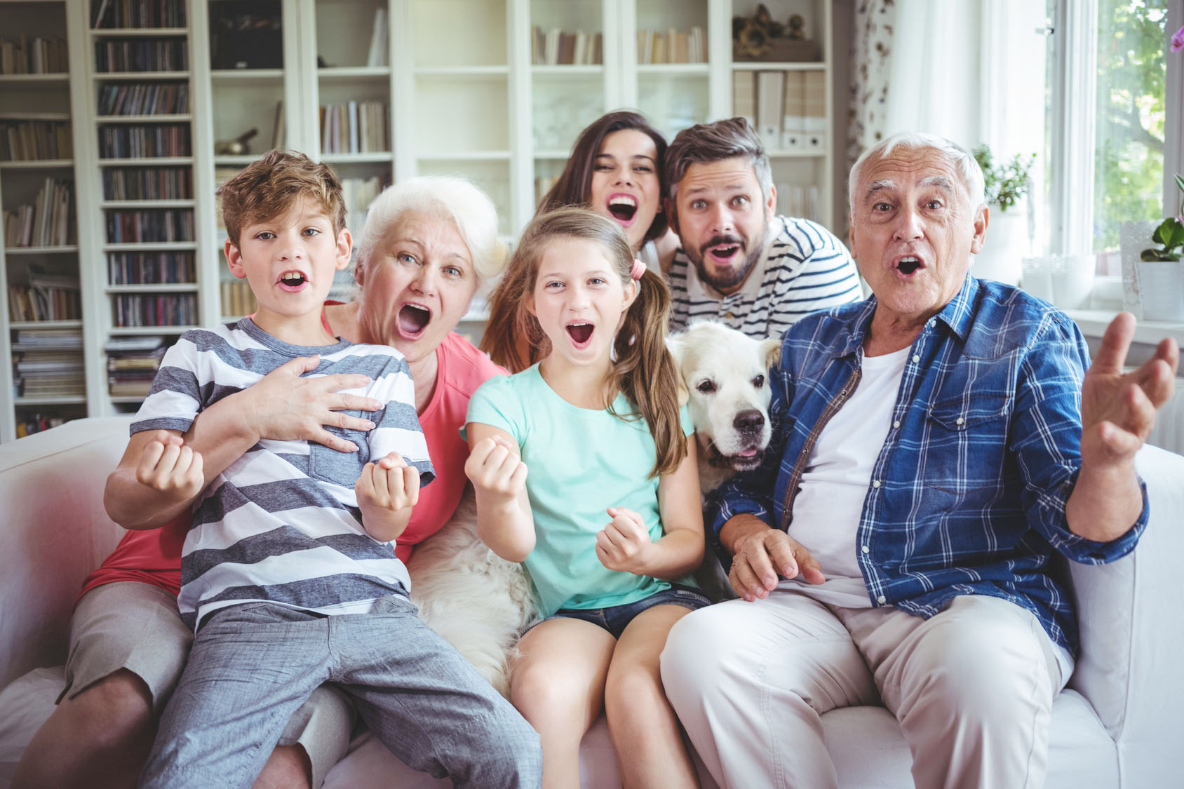 Familienbild: 3 Generationen sitzen mit Hund auf Couch im Wohnzimmer