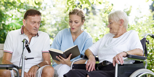 Betreuerin liest älteren Menschen ein Buch vor